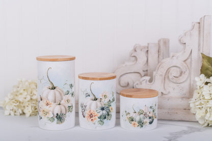 Three decorative bathroom canisters with floral and pumpkin designs on a white surface.