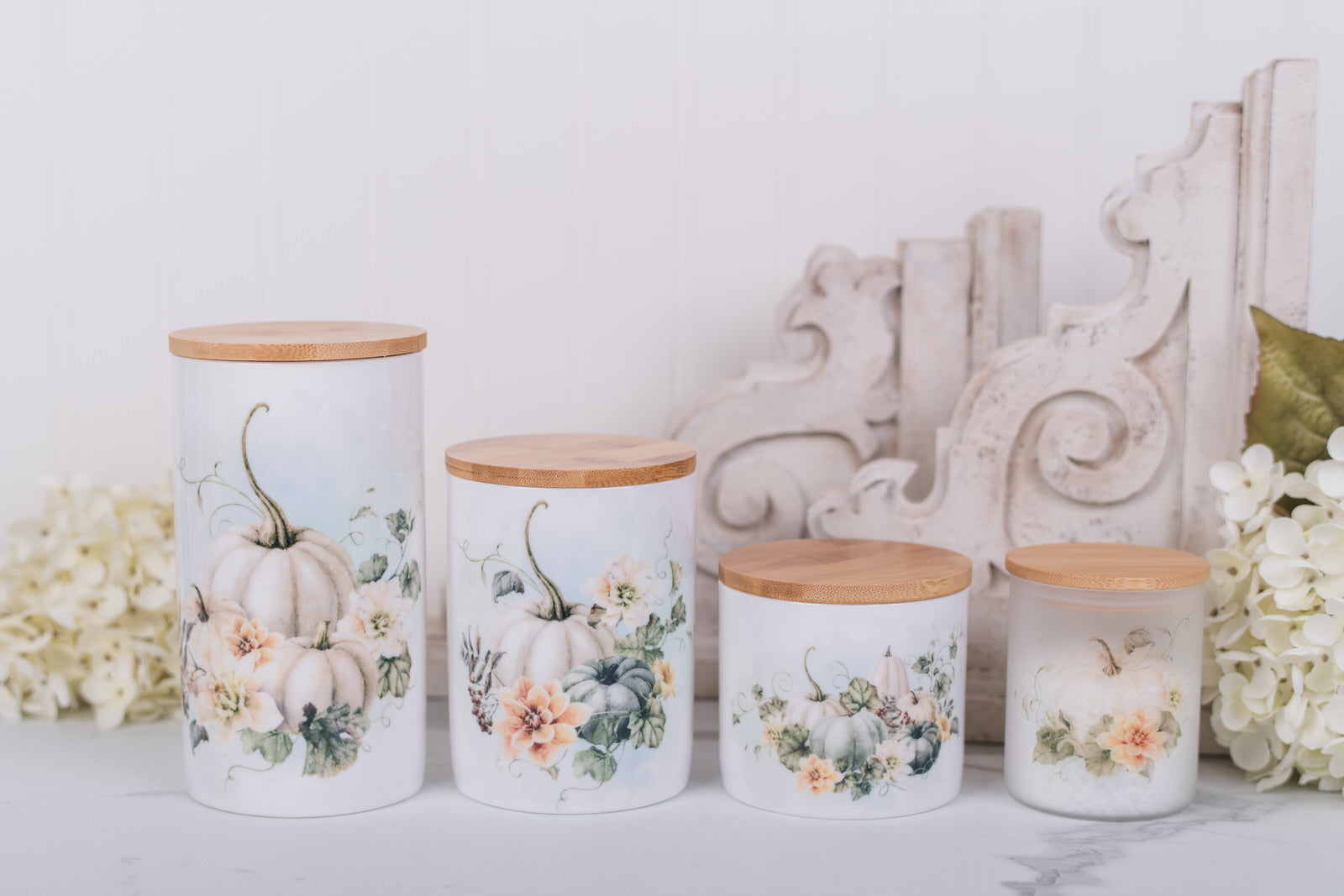 Set of four decorative canisters with floral and pumpkin designs on a white surface.