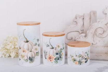 Three decorative canisters with floral and pumpkin designs on a white surface.