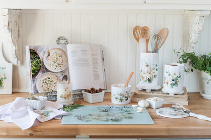 A kitchen counter styled for fall with cookbooks, utensils, a cutting board and decorative items on a wooden surface.
