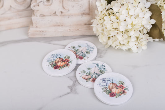 Four round coasters with floral designs and scripture on a marble surface with white flowers.