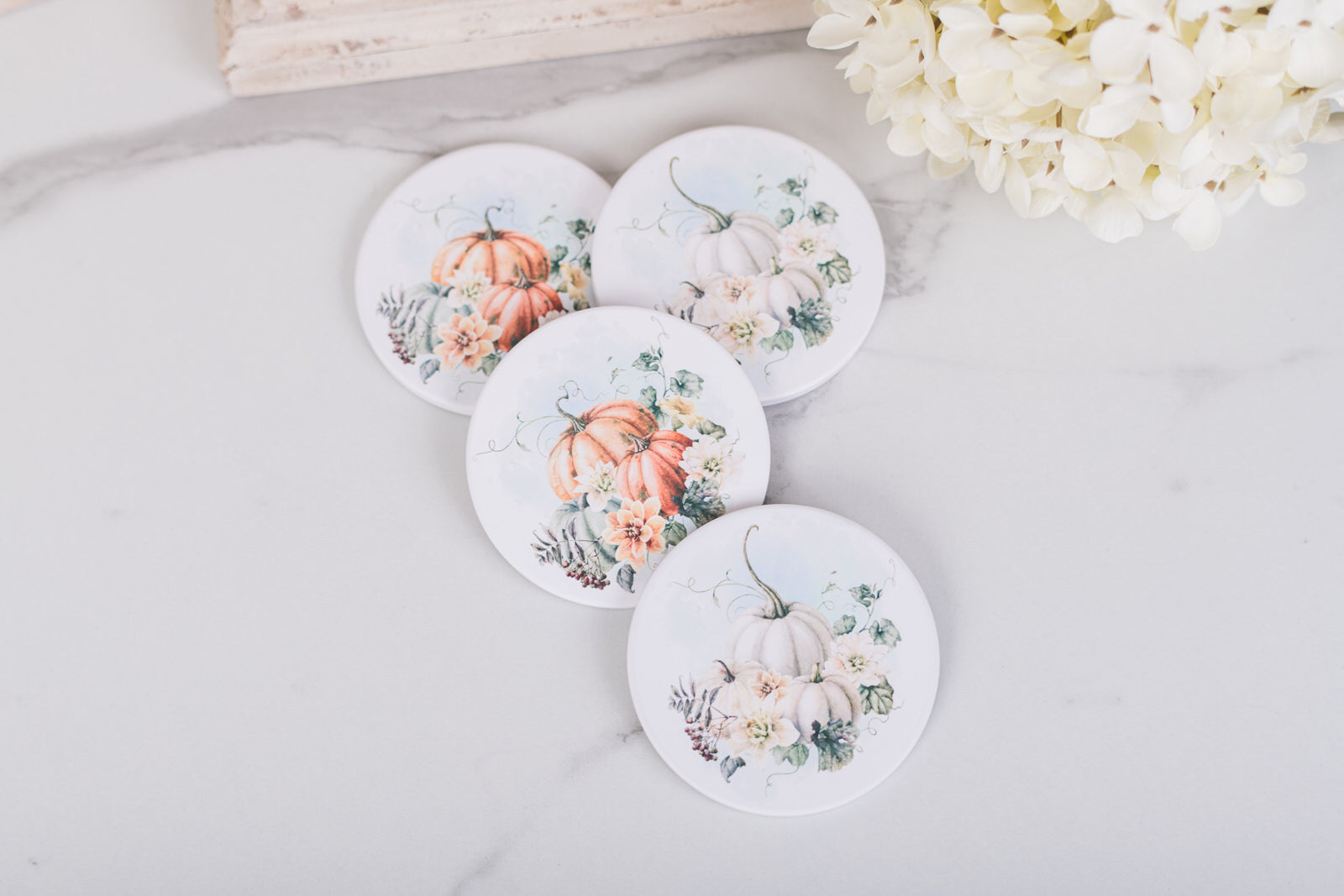 Set of four round coasters with pumpkin and floral designs on a light surface.