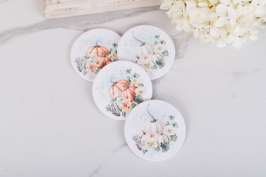 Set of four round coasters with pumpkin and floral designs on a light surface.