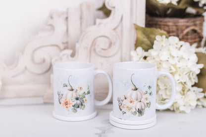 Two white mugs with pumpkin and floral designs on a marble counter