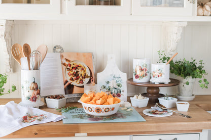 Kitchen counter with squash in a casserole dish on a glass cutting board and decorative autumn items on a wooden surface.