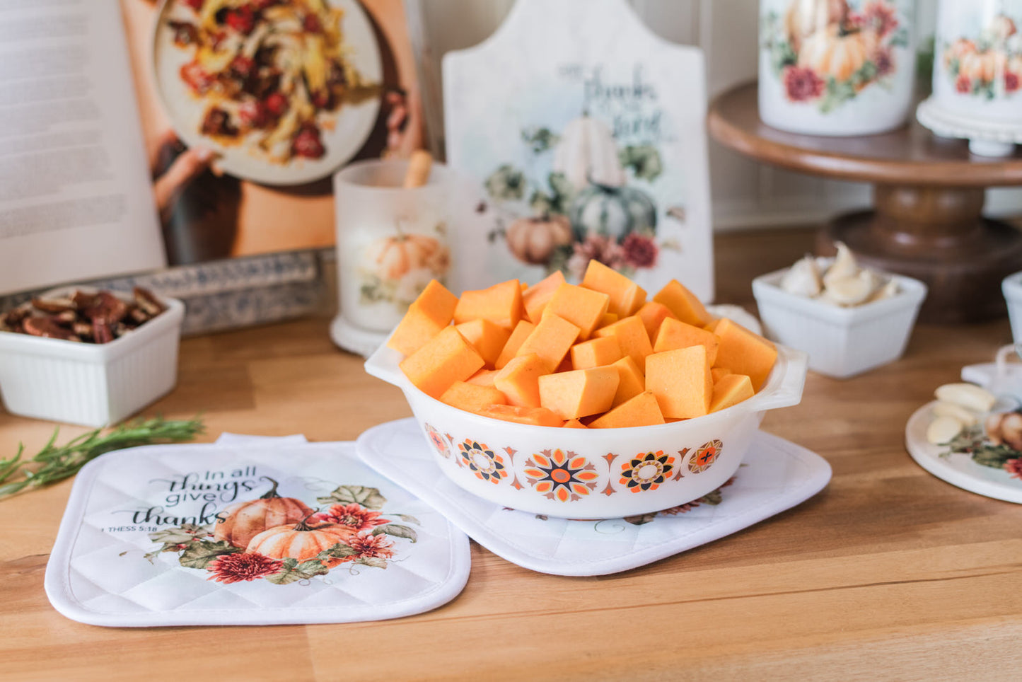 Diced butternut squash in a vintage-style bowl on a butcher block protected with fall scripture pot holders with decorative items.
