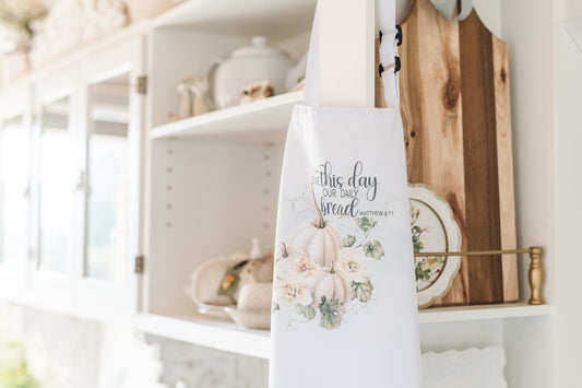 Soft fall apron with pumpkin design and Matthew 6:11 scripture, hanging in a kitchen