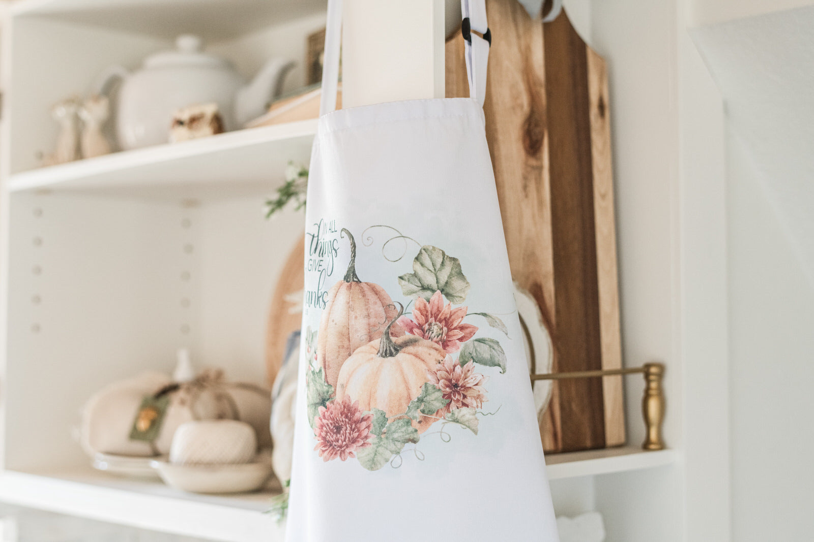 Floral apron hanging on a wooden hook in a kitchen setting with shelves and decor.