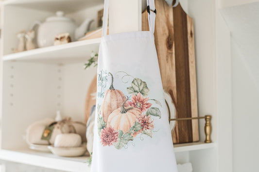 Floral apron hanging on a wooden hook in a kitchen setting with shelves and decor.