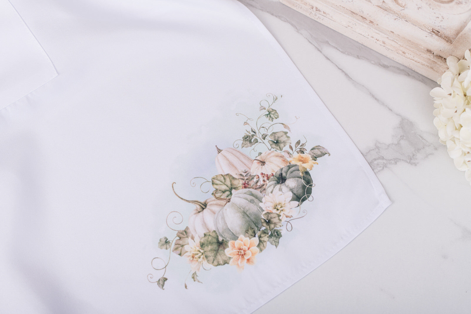 Floral and pumpkin design on a white apron in the lower corner 