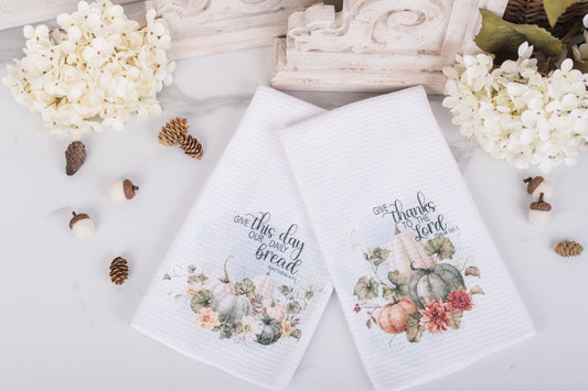 Two decorative towels with floral designs and scripture on a white surface with decorative elements.
