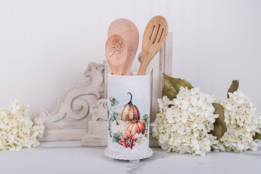 Ceramic utensil holder with wooden spoons on a decorative surface with flowers 