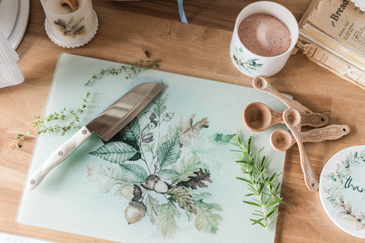 Fall glass cutting board with floral design on a wooden table with kitchen items.