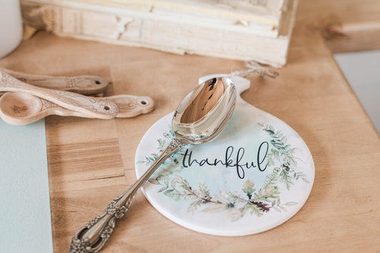 Spoon on a decorative coaster with 'thankful' text on a wooden surface