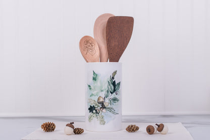 Decorative kitchen utensil holder with wooden spoons on a light background. Leaf and acorn design.
