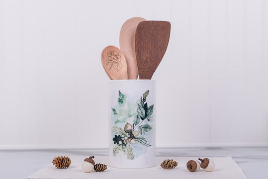 Decorative kitchen utensil holder with wooden spoons on a light background. Leaf and acorn design.