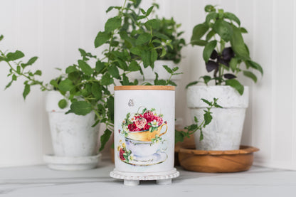 Decorative plant pot with floral design in front of potted plants on a white surface