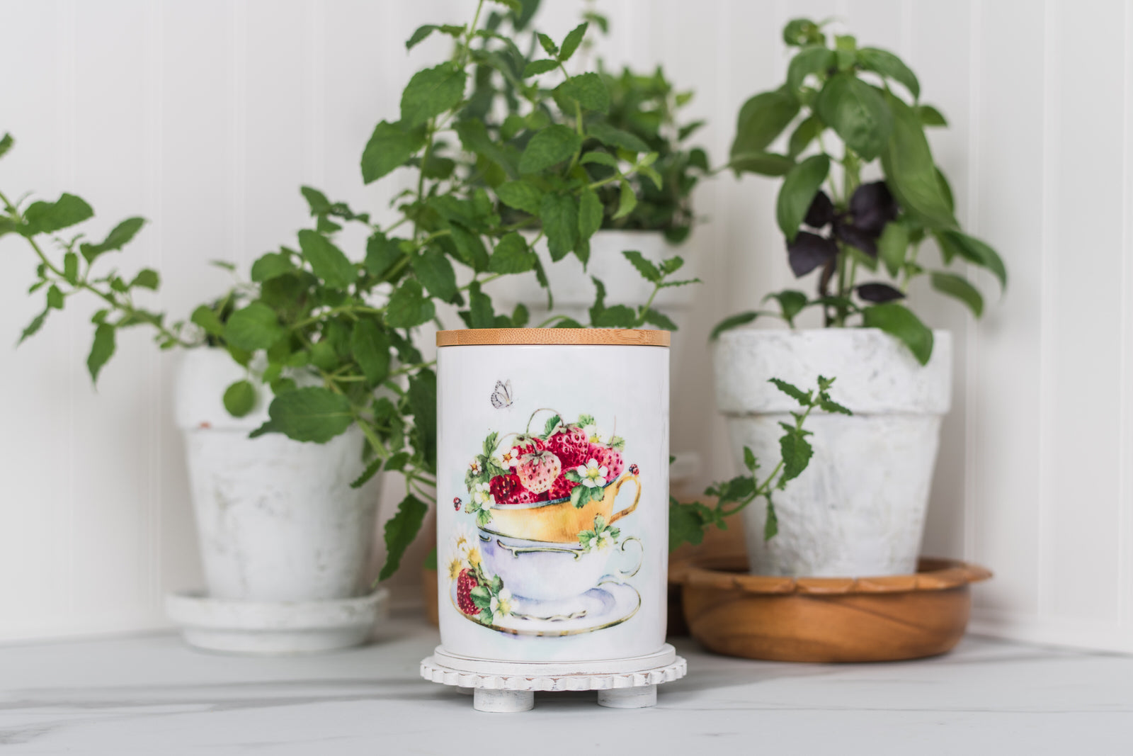 Decorative bathroom jar with floral design in front of potted plants on a white surface