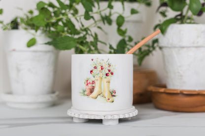 Decorative jar with floral design on a white surface with plants in the background
