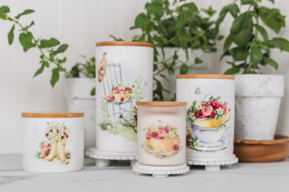 Set of decorative jars with floral designs on a white surface with plants in the background