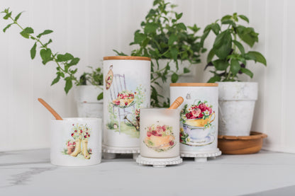 Decorative canisters with floral designs on a surface with plants in the background