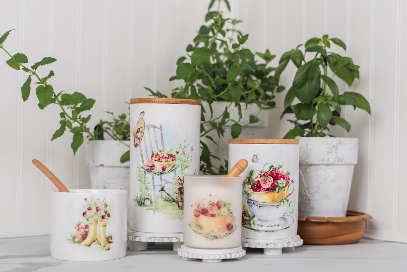 Set of ceramic canisters with decorative designs on a white surface with plants in the background