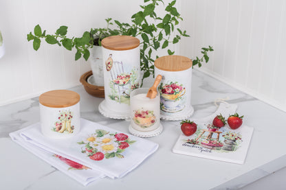 Decorative kitchen canisters with floral designs on a countertop with plants and towels.