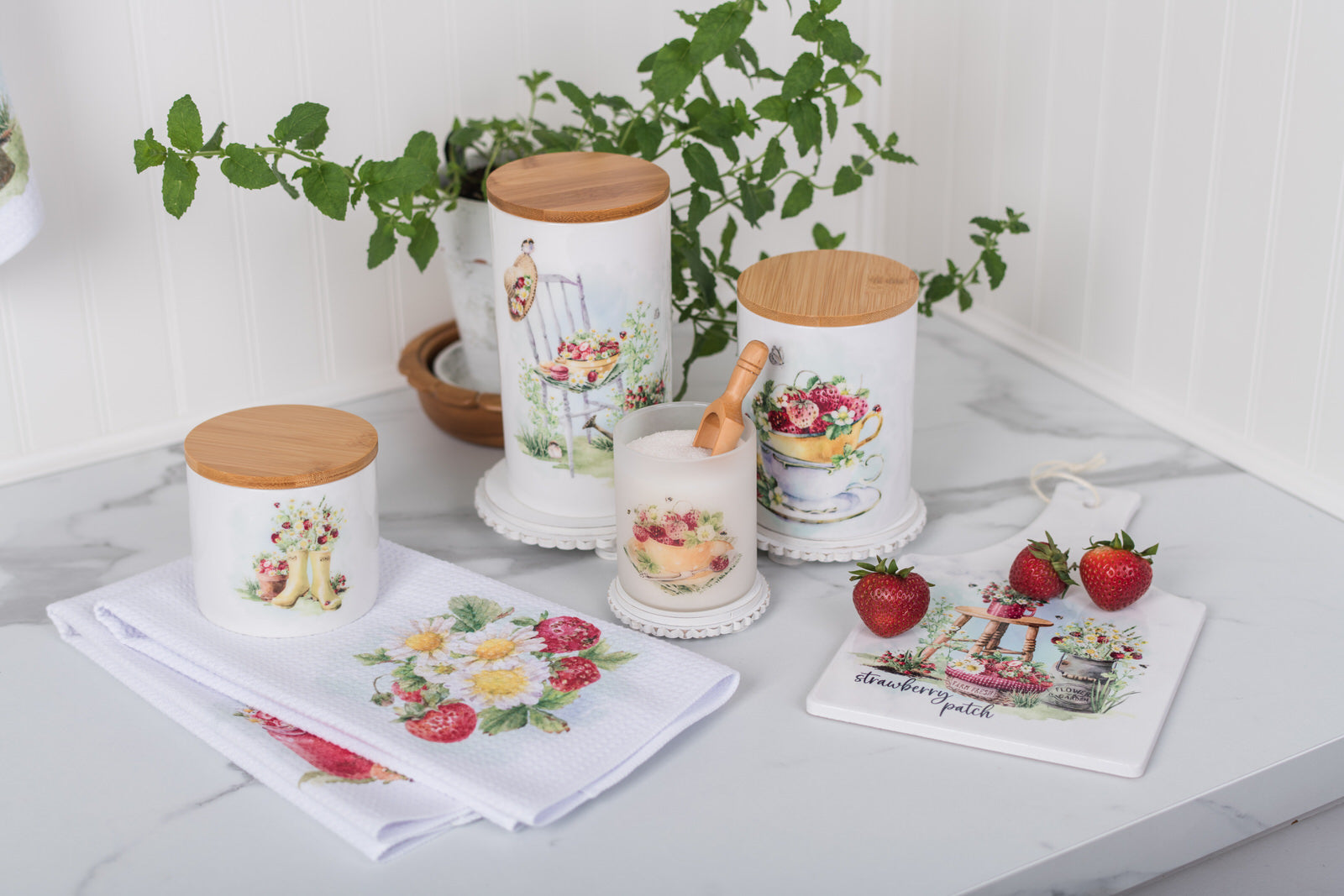 Decorative bathroom canisters with floral designs on a countertop with a plant in the background.