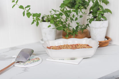 Baked dish in a white dish on a table with potted plants in the background