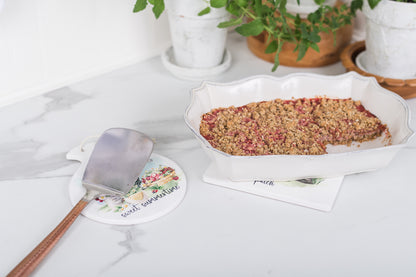 Baked dish in a white dish with a spatula on a table with plants in the background