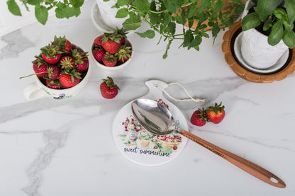 Table setting with strawberries, a spoon, and a decorative spoon holder on a marble surface.