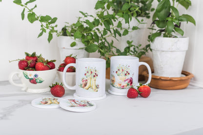 Two white mugs on coasters with floral designs on a table with strawberries and plants in the background