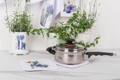 Stainless steel pot with black handle on a white surface, surrounded by potted plants and decorative items.