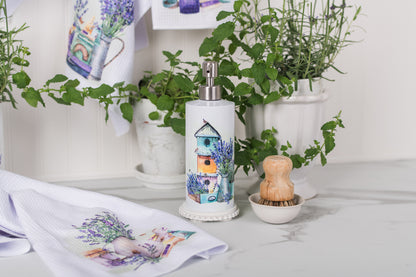 Decorative soap dispenser with a birdhouse design on a table with plants and towels.