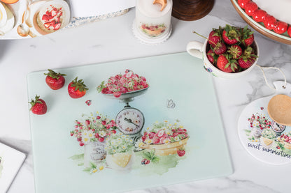 Glass cutting board with floral design on a table with strawberries and tea cups.