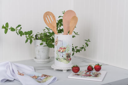 Kitchen utensil holder with wooden spoons on a table with decorative items.