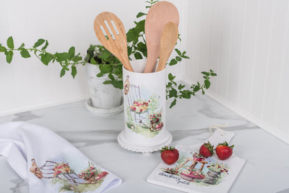 Decorative kitchen utensil holder with wooden spoons on a marble surface with plants and strawberries.