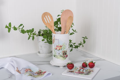 Kitchen utensil holder with wooden spoons on a countertop with strawberry themed decorative items.