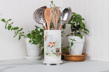 Kitchen utensil holder with utensils on a white surface with plants in the background
