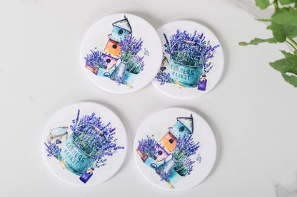 Four coasters with lavender and birdhouse designs on a white surface.