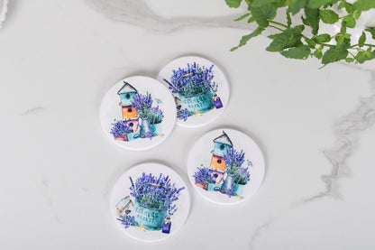 A set of four white ceramic coasters with a floral design and a French lavender theme, featuring a house and lavender bushes.