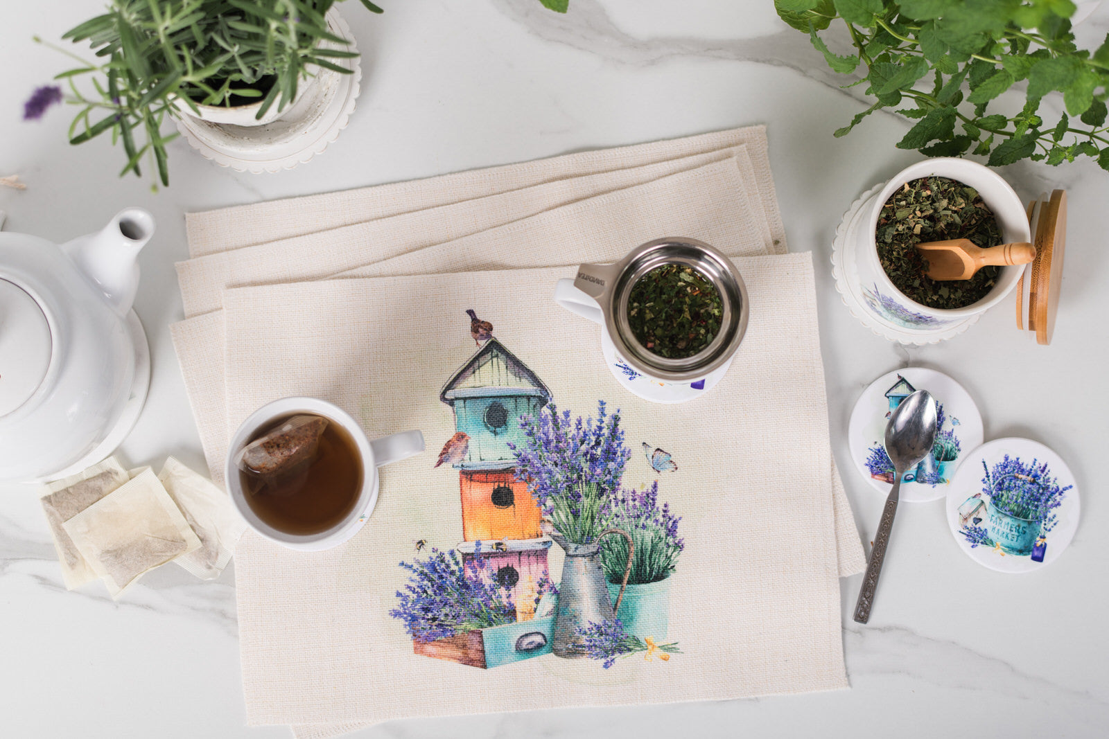Tea set with a decorative mat featuring birdhouses and lavender on a white surface.