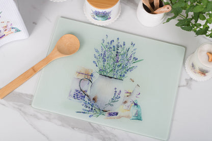 Glass cutting board with floral design on a marble surface with a wooden spoon and plant.