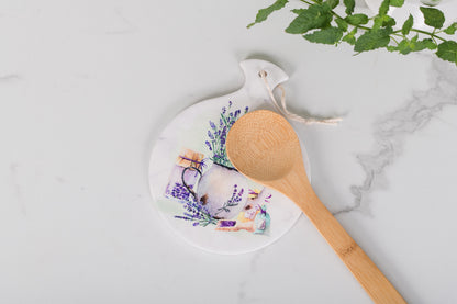 Round white trivet with floral design and wooden spoon on a marble surface