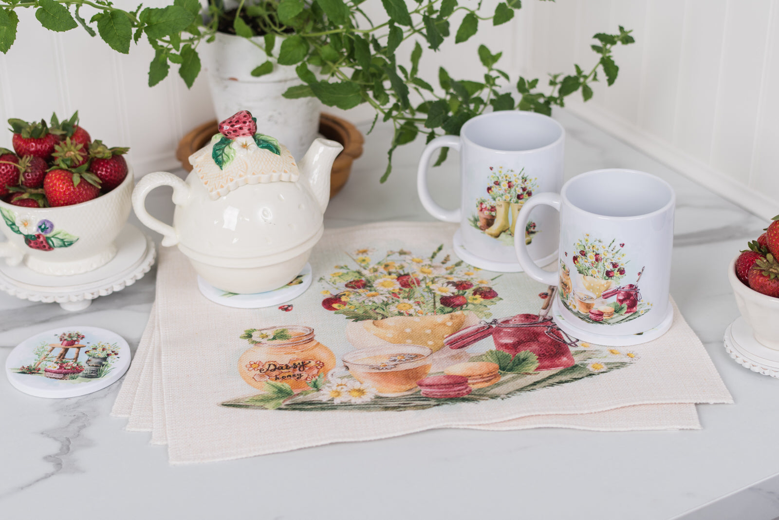 Tea set with mugs, teapot, and strawberries on a table with decorative placemats.