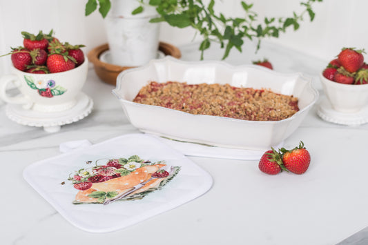Strawberry crumble dessert in a baking dish with fresh strawberries on a table beside potholders 