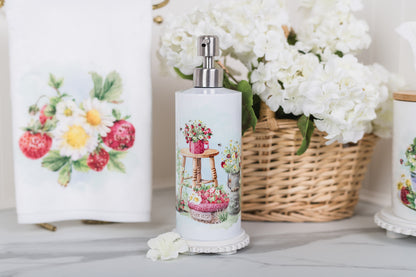 Decorative soap dispenser with floral design next to a basket of flowers on a wooden surface.
