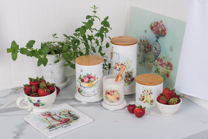 Decorative kitchen items including jars, a teacup, and strawberries on a table with a plant and strawberry-themed cutting board in the background.