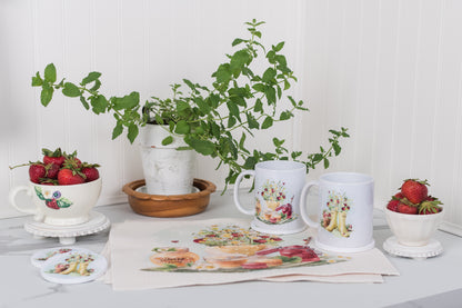 Two mugs with floral designs on a table with strawberries and a plant.