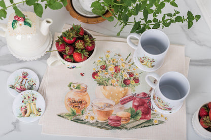 Tea set with cups, teapot, and coasters on a tablecloth with fruit and floral design.